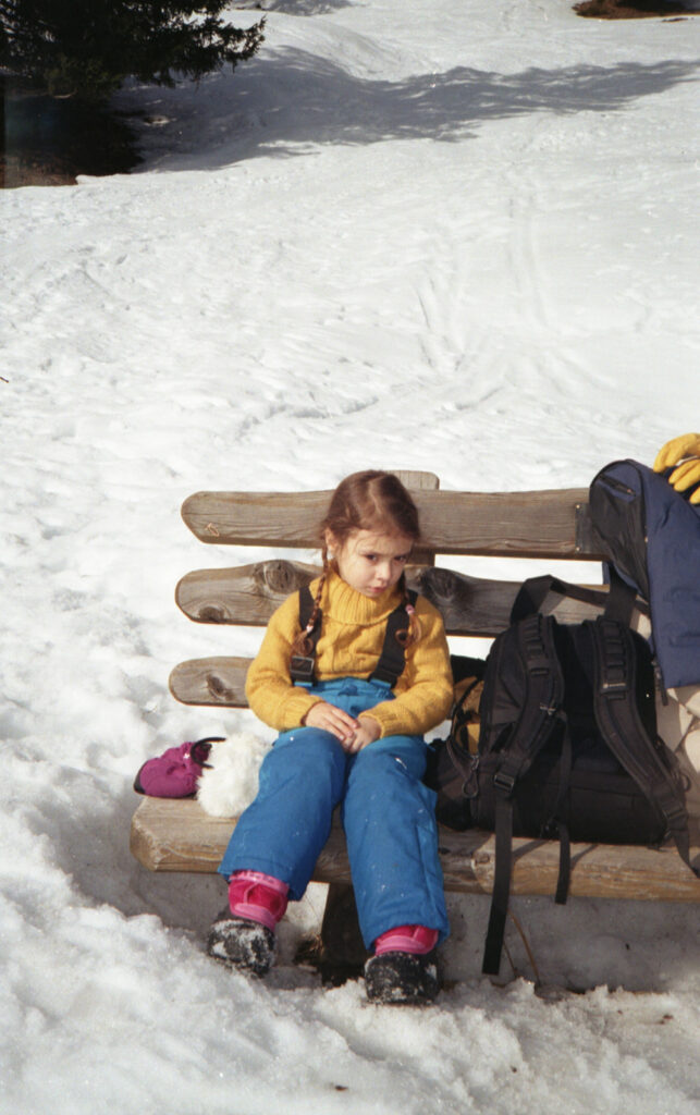 petite fille assise sur un banc entouré de neige dans une tenue de ski pour la luge