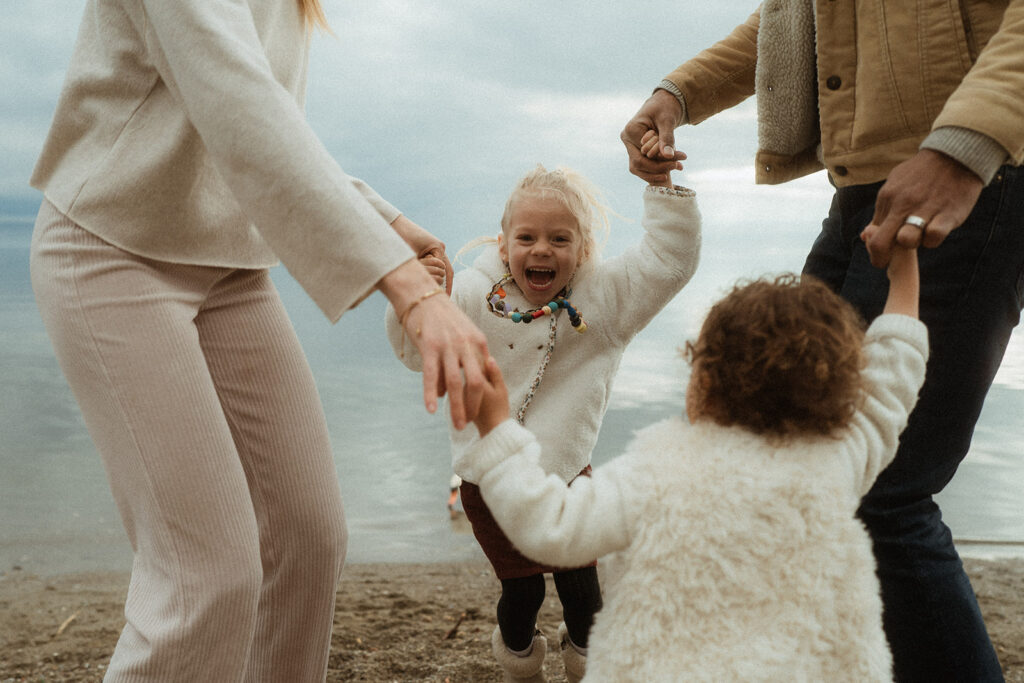 Une famille avec deux enfants qui se tiennent les mains et sautent en rond en rigolant. Shooting photo en famille à vidy